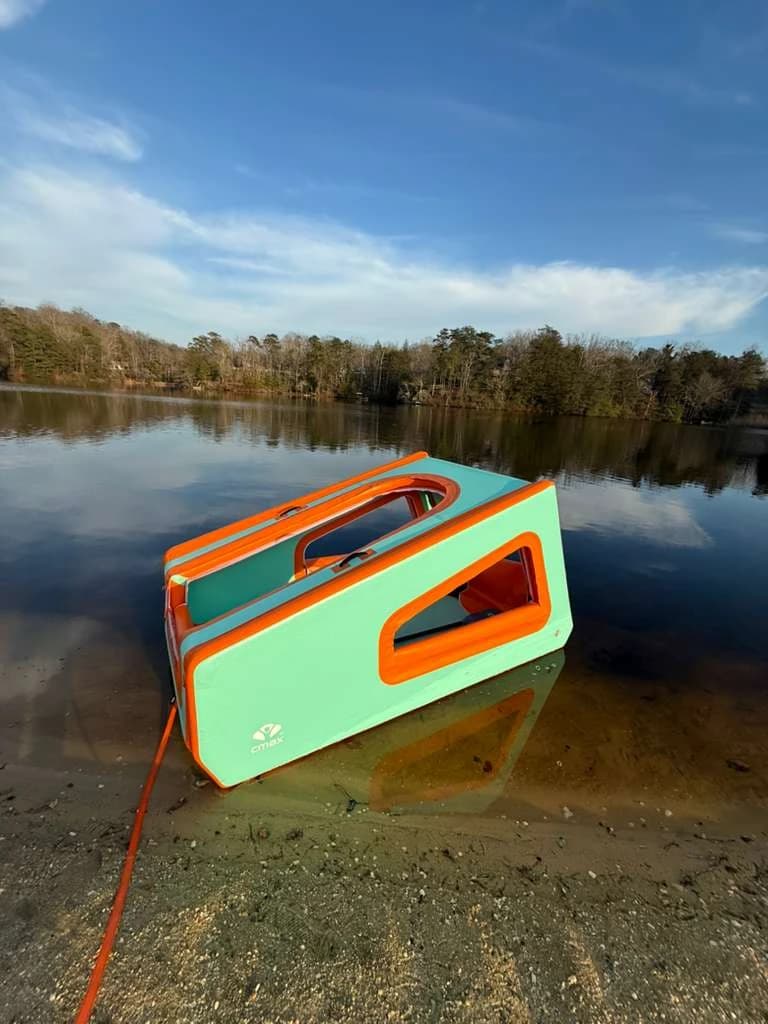 Turquoise and orange AeroCabin at the edge of a lake in daylight.