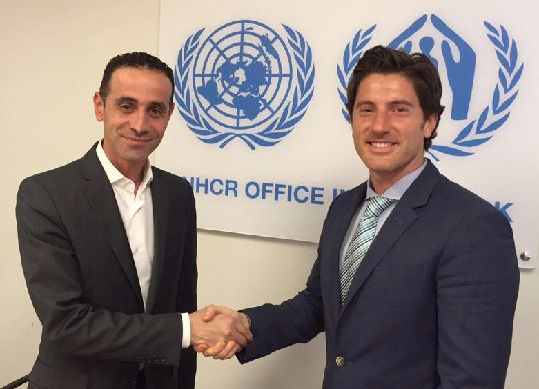 Nicolás García Mayor and a meeting participant shaking hands in front of UNHCR office signage.
